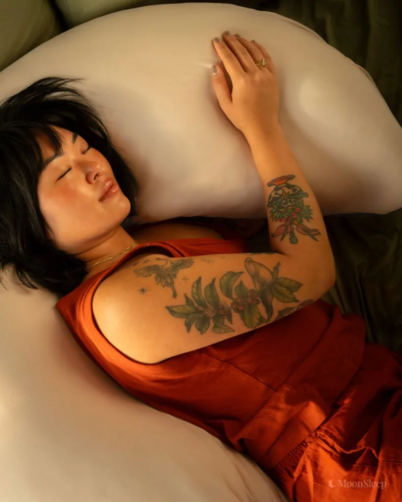 Asleep with her arm wrapped around a champagne MoonSpoon™ body pillow